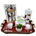 A gift basket containing decorative candles, hand cream collection, wipes, mini cologne spray, lip therapy kit, and an artificial flower pot, all arranged in a basket with a cellophane wrap.
